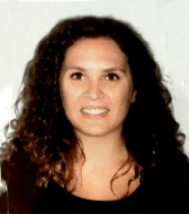 Sabrina Armenio. Una mujer con cabello largo, rizado y oscuro sonríe a la cámara. Lleva una blusa oscura y está colocada sobre un fondo liso y de color claro.