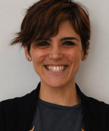 Yone Castillo. Una mujer de pelo corto y castaño y que viste una chaqueta oscura sonríe ampliamente a la cámara. El fondo es de color claro y liso.