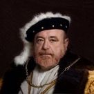 Un hombre está vestido con un elaborado atuendo de estilo renacentista, que incluye un sombrero de plumas blancas y negras y una capa ricamente adornada con cadenas de oro alrededor de su cuello. Tiene una expresión seria y una barba bien cuidada. El fondo es oscuro.